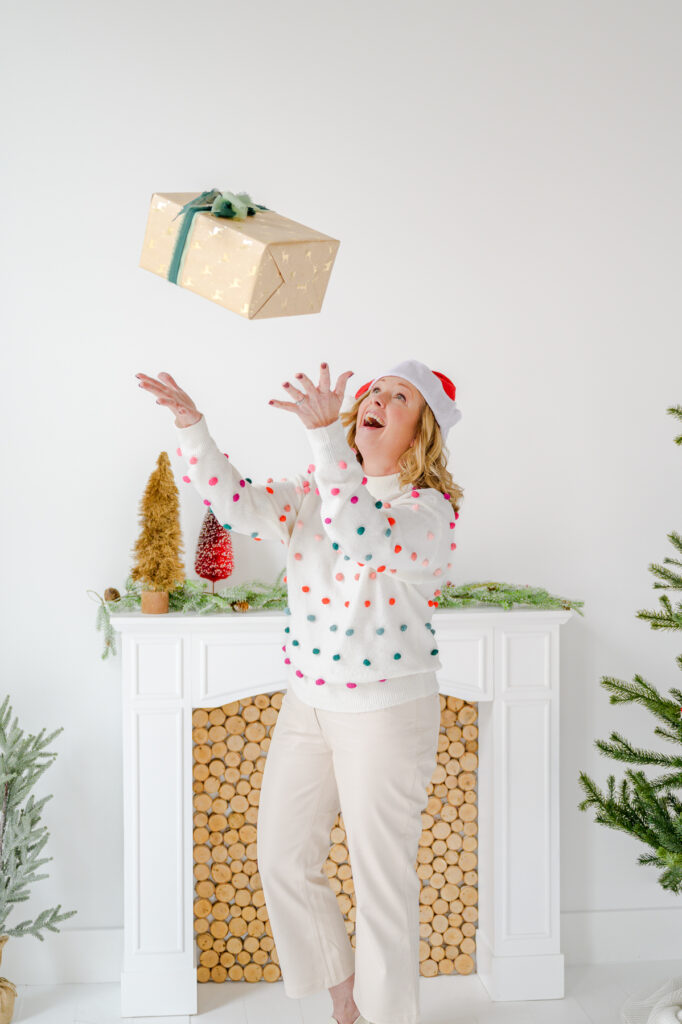 realestate agent getting some holiday brand photography content photos taken. she's in a santa hat and fun sweater in a natural light studio. taken by a professional business photographer and personal brand photographer for elevated content