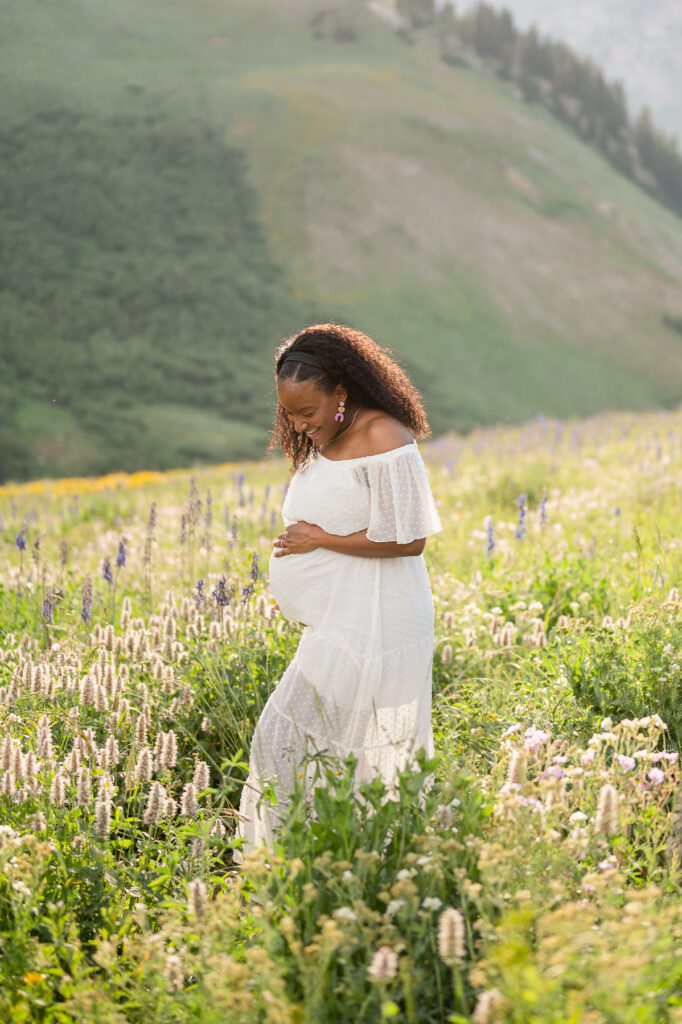 photo of a woman posing for maternity photos in the wildflowers up little cottonwood canyon for family pictures taken by luxury utah family photographer
